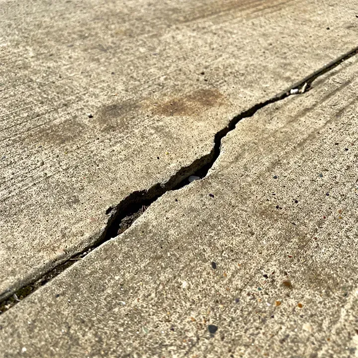 Close-up of a crack running across an aging concrete driveway slab on a sunny day.