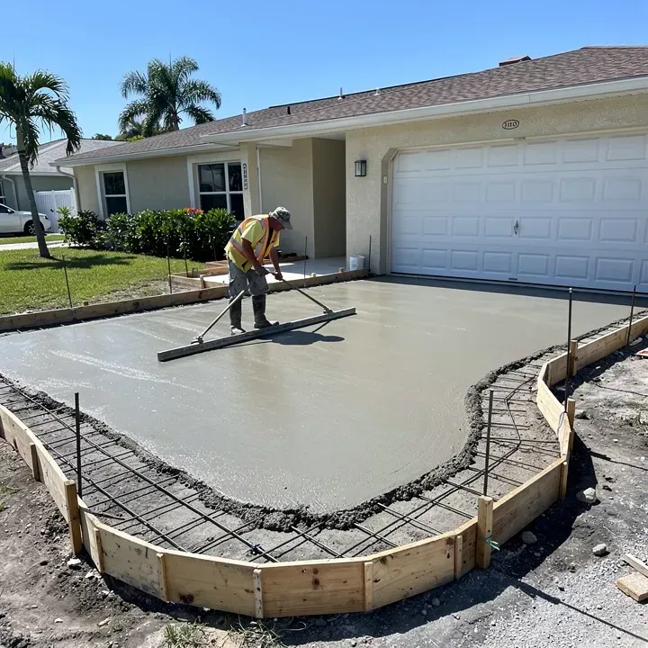 Concrete driveway pour in progress at a Lake Worth, Florida home, worker shown from behind on a sunny day.