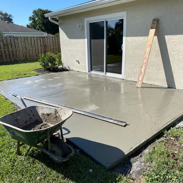 Concrete patio being finished at a Lake Worth, Florida home, empty wheelbarrow and tools nearby on a sunny day.