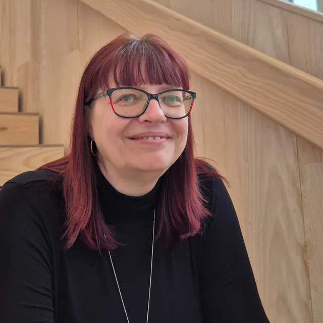 Marion Schumann lächelt warm auf einer Holztreppe, Mentorin für Mut und Empowerment bei Lipödem