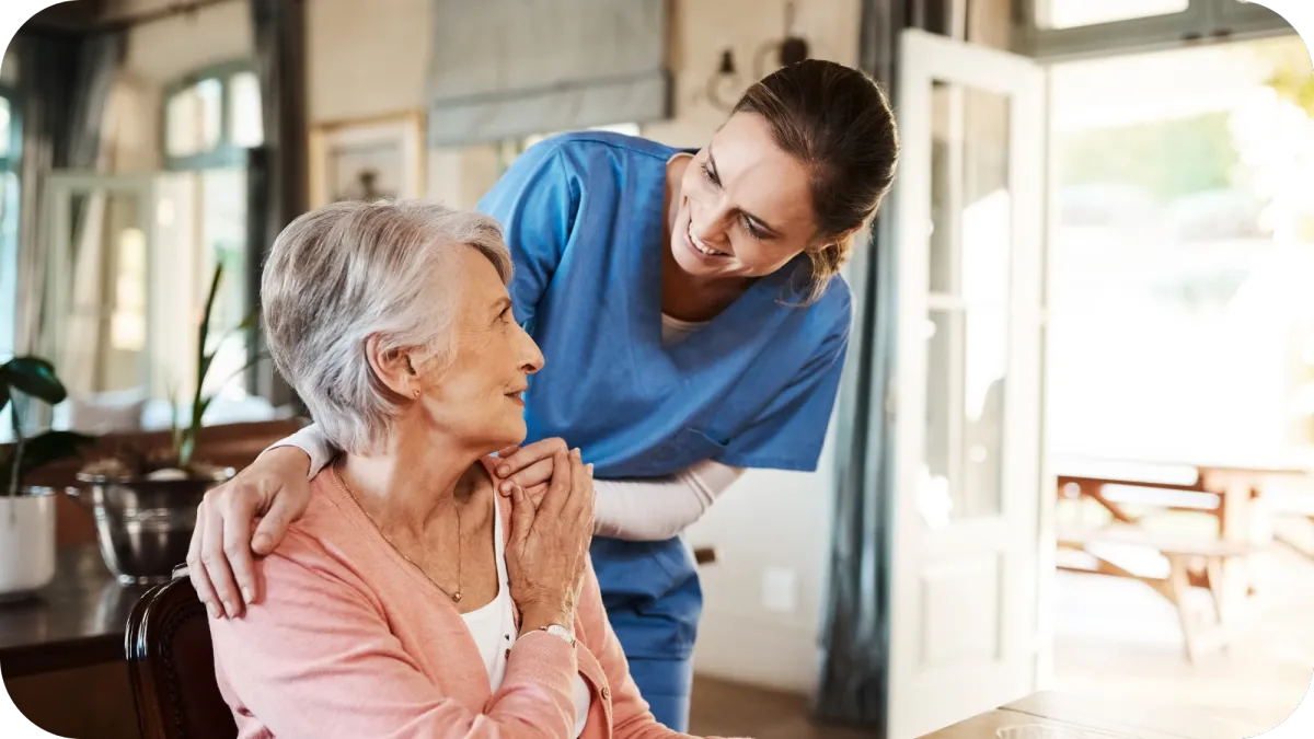 A compassionate caregiver smiling and talking with an elderly woman, showing personalized senior care and support in a home environment.