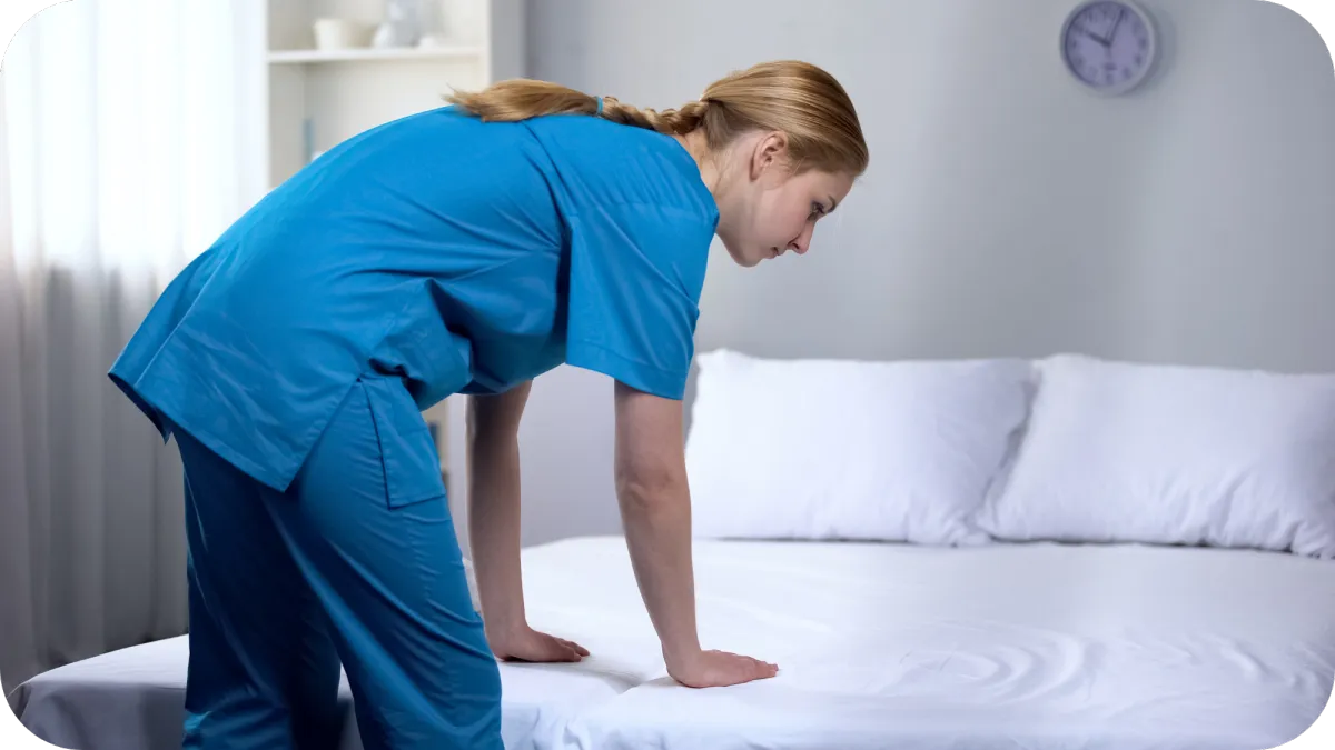 A caregiver in blue scrubs making a fresh bed, representing diligent home health and patient care services.