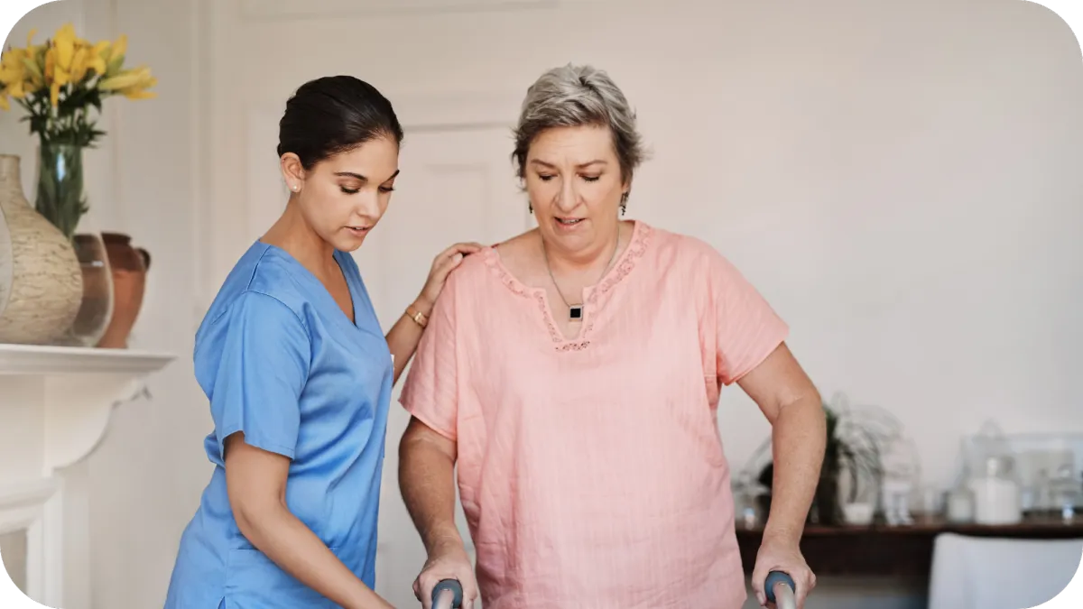 A caregiver in blue scrubs providing support to a senior woman using a walker, highlighting dedicated home health assistance.