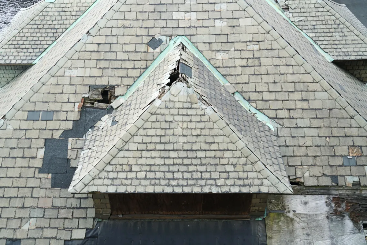 A storm damaged roof that is missing shingles and has some holes in it.