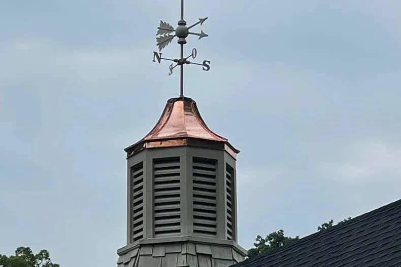 A roof with a brass decorative element on it. The brass element has a metal compass on top of it.