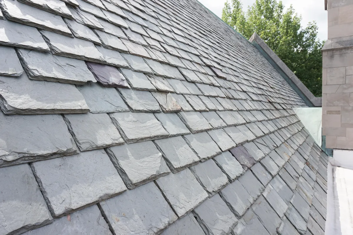 A picture of gray, slate shingles on top of a steep roof on a sunny day.