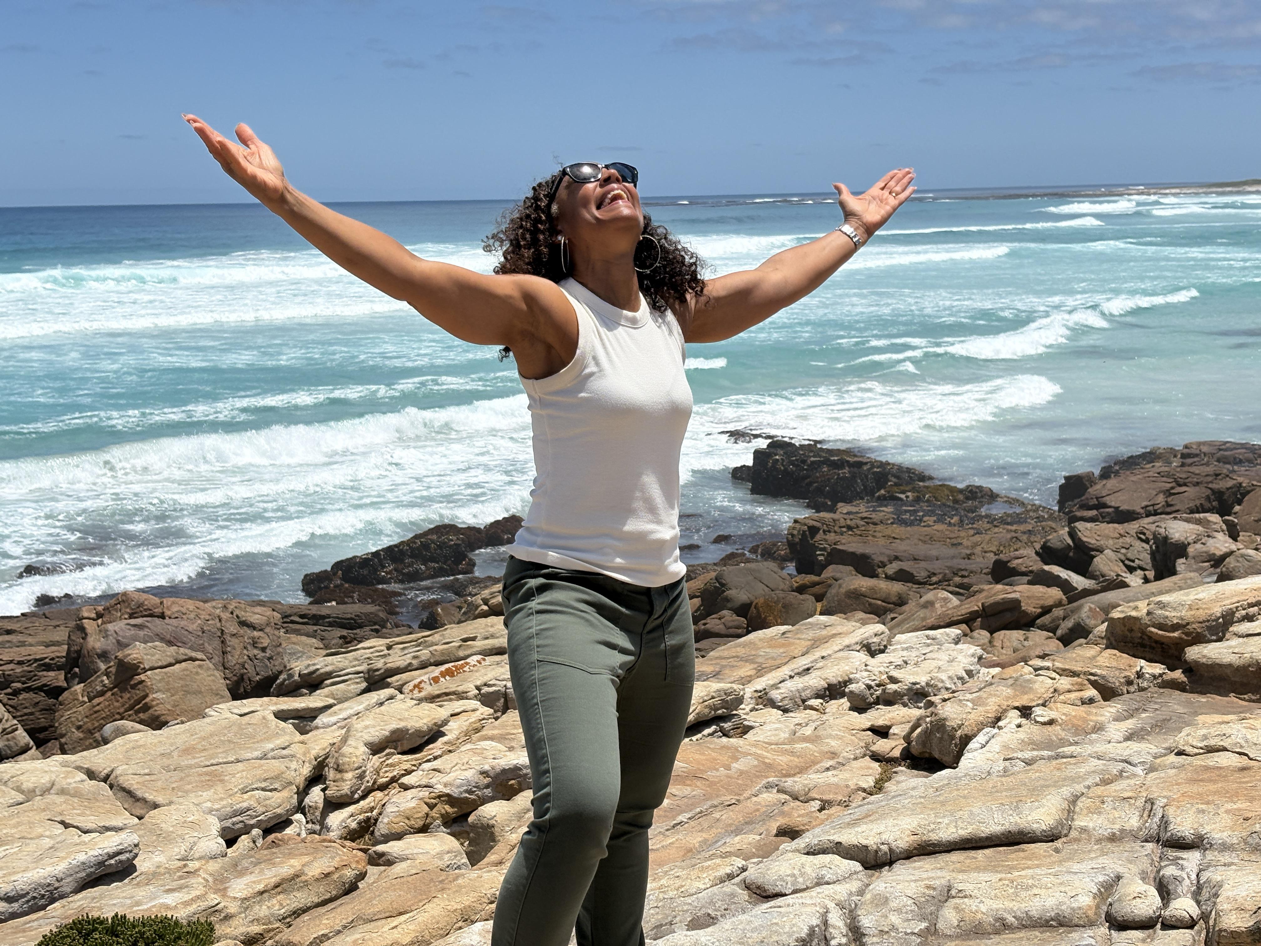 A close-up of a gentle hand reaching out to another, both hands belonging to women of different backgrounds. The background is softly blurred, with warm neutral tones, symbolizing support and connection.