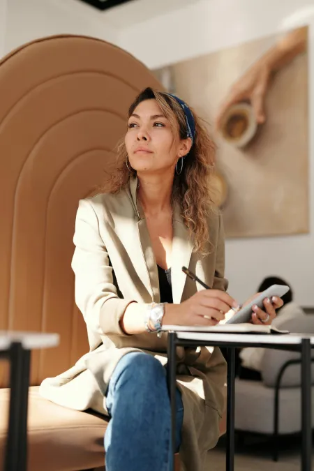 Woman sitting at a small table, deep in thought with pen in hand — symbolising clarity, planning, and creative focus