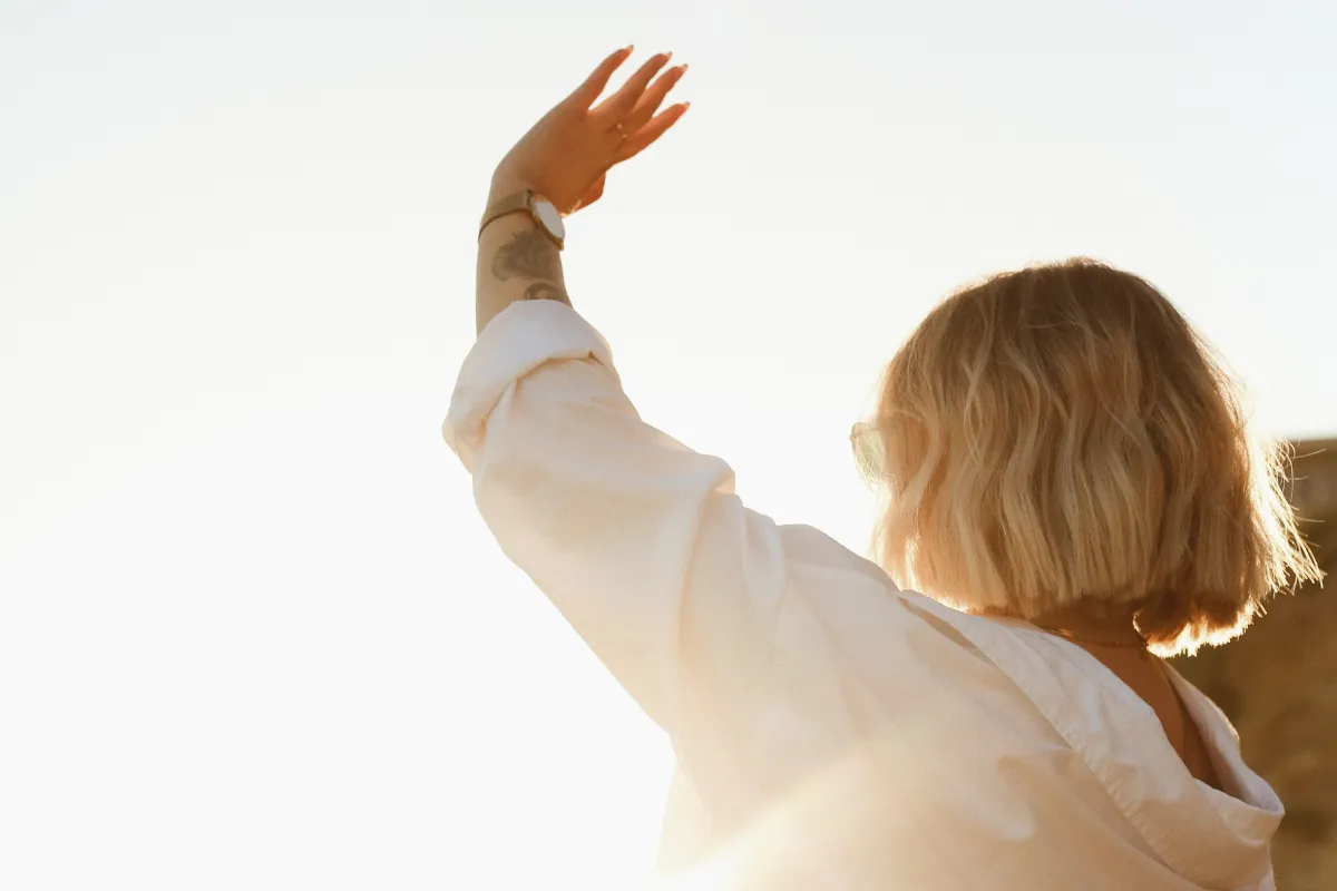 Woman looking up into the sunlight with hand raised — representing hope, collaboration, and the future of solopreneurship.