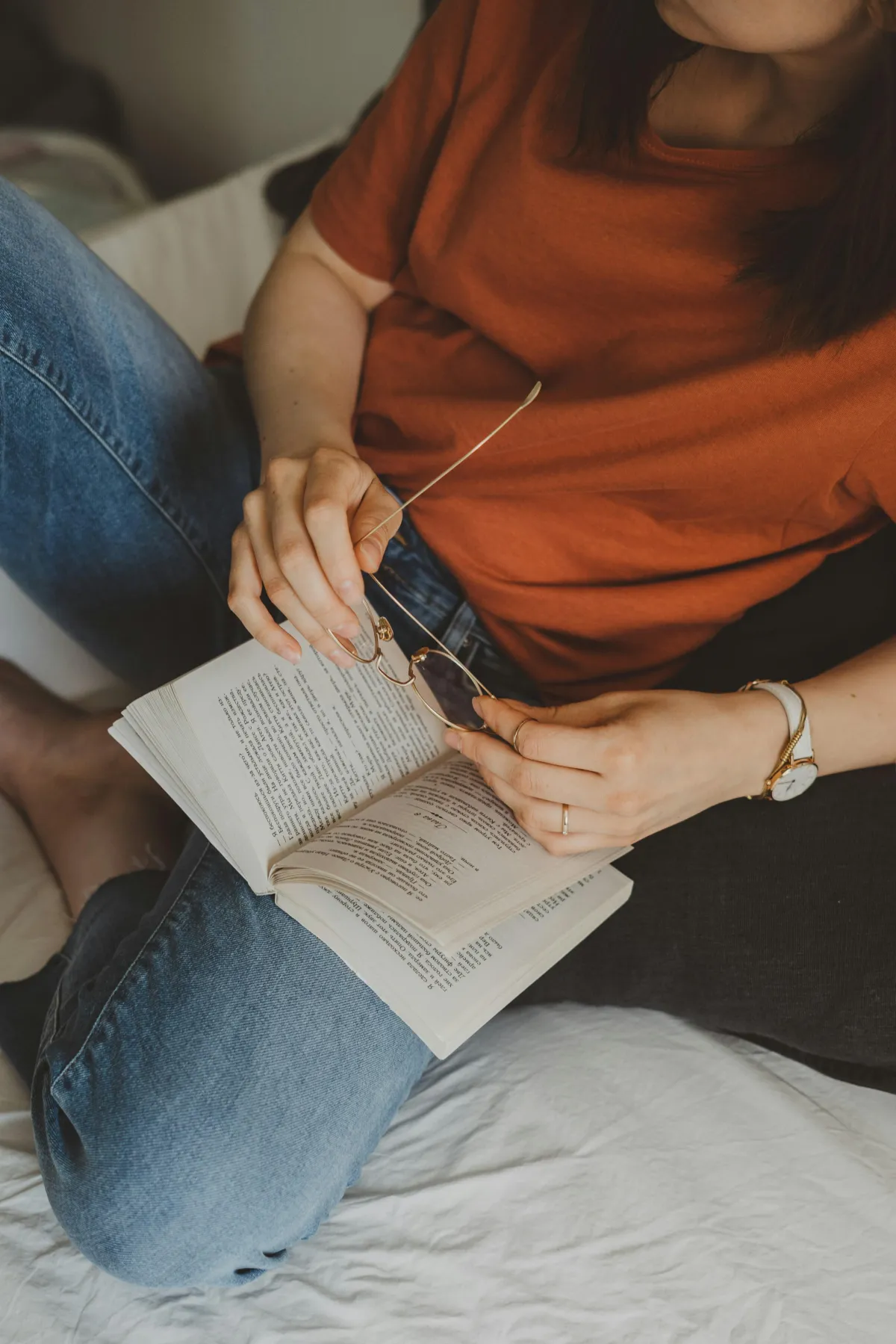 Woman sitting on a bed with glasses and an open book, symbolising reflection, trust, and calm momentum in business.