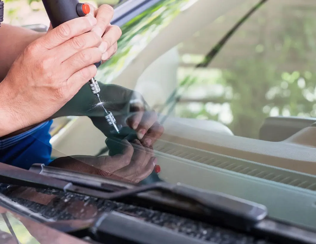 Technician repairing a windshield chip with precision tools in the field