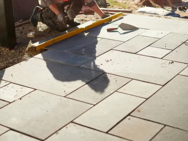  Worker installing a paver patio, using a level to ensure even placement.