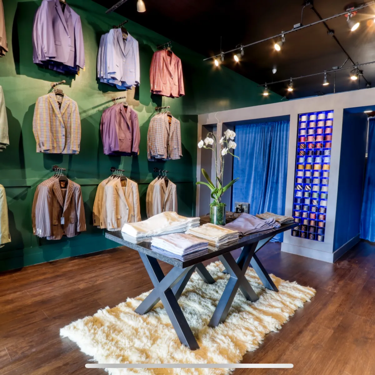 Inside The House of Suits in Coral Gables, FL, a luxurious display of Italian suits adorns the wall, exuding elegance and sophistication. A meticulously arranged table presents a diverse selection of dress pants, available in various colors, patterns, and high-quality materials, perfect for any occasion. The impressive assortment of ties on the wall contributes to the store's bespoke feel, showcasing an array of intricate designs, rich textures, and fashion-forward colors, ensuring an impeccable and well-coordinated ensemble for every refined individual.