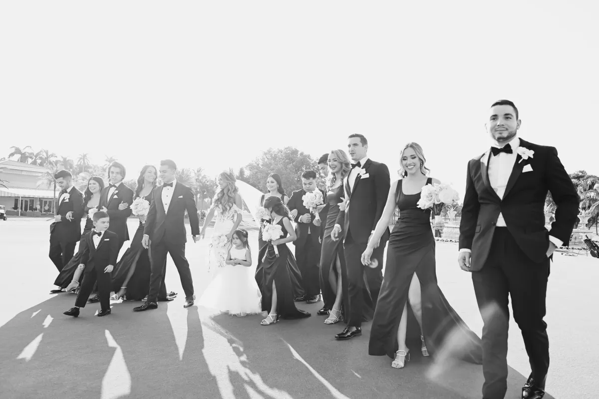 An exciting moment captured as the entire wedding party, consisting of groomsmen and bridesmaids, walks down the aisle with smiles on their faces. The groomsmen can be seen wearing their stylish suits from The House of Suits, tailored to fit them perfectly. Each suit has a unique touch, like a colorful tie, pocket square, or lapel pin.