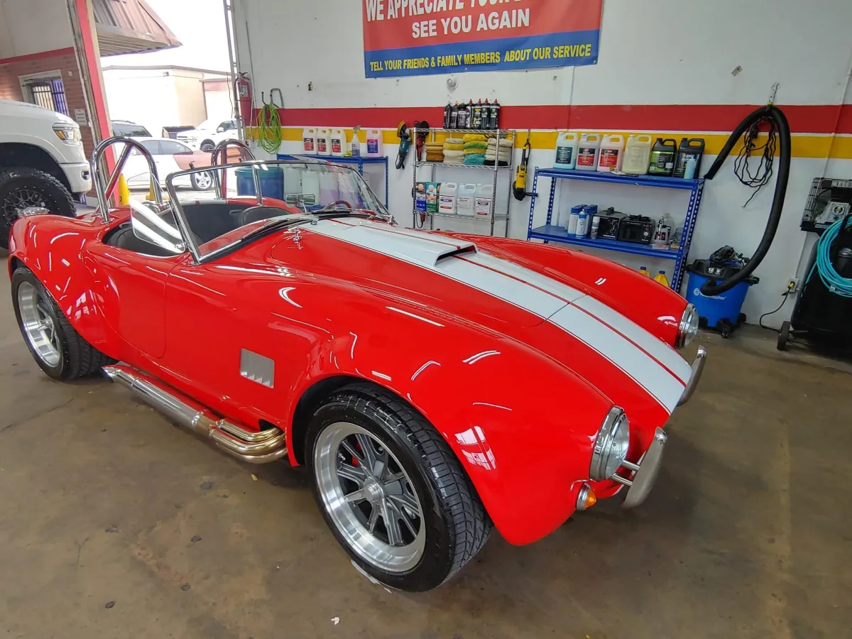 Red sports car with white stripes in a detailing shop, showcasing high-quality vehicle care and restoration services.