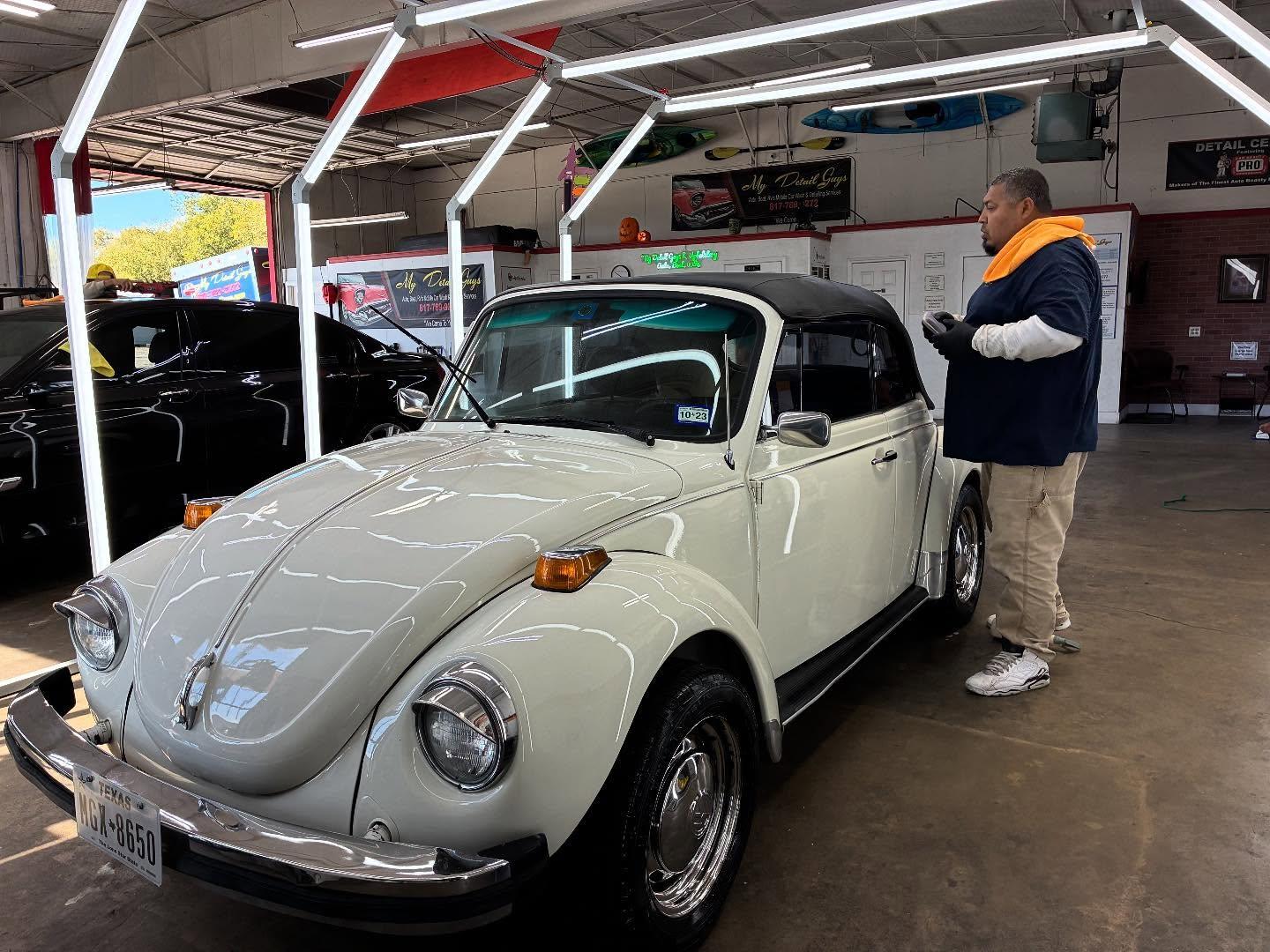 Mobile car detailing service employee working on a classic white Volkswagen Beetle in a detailing shop, showcasing the attention to interior and exterior care.