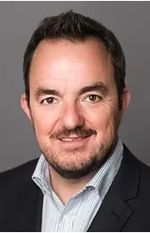 Portrait of a white woman with short hair, standing in a collaborative workspace, holding a notepad, surrounded by brainstorming notes. 3:2 aspect ratio, candid, energetic vibe.