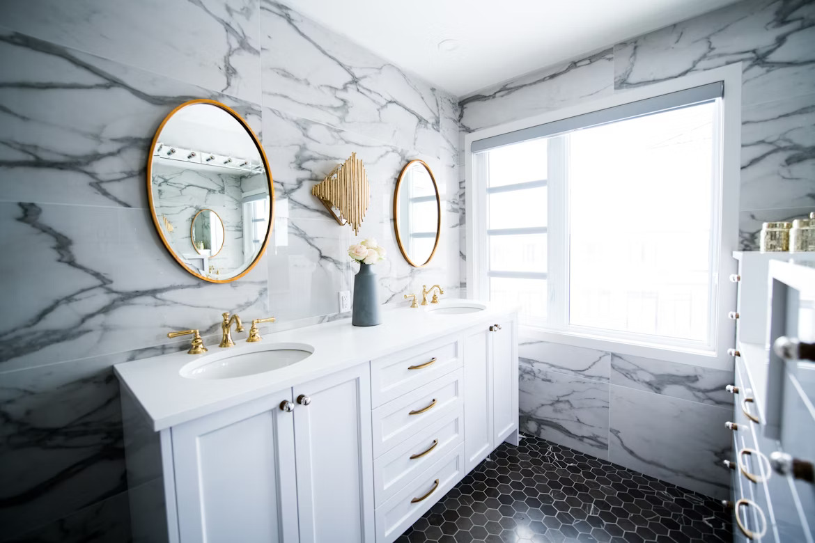 white marble walls with black hexagon tiles with two gold framed mirrors and white vanity
