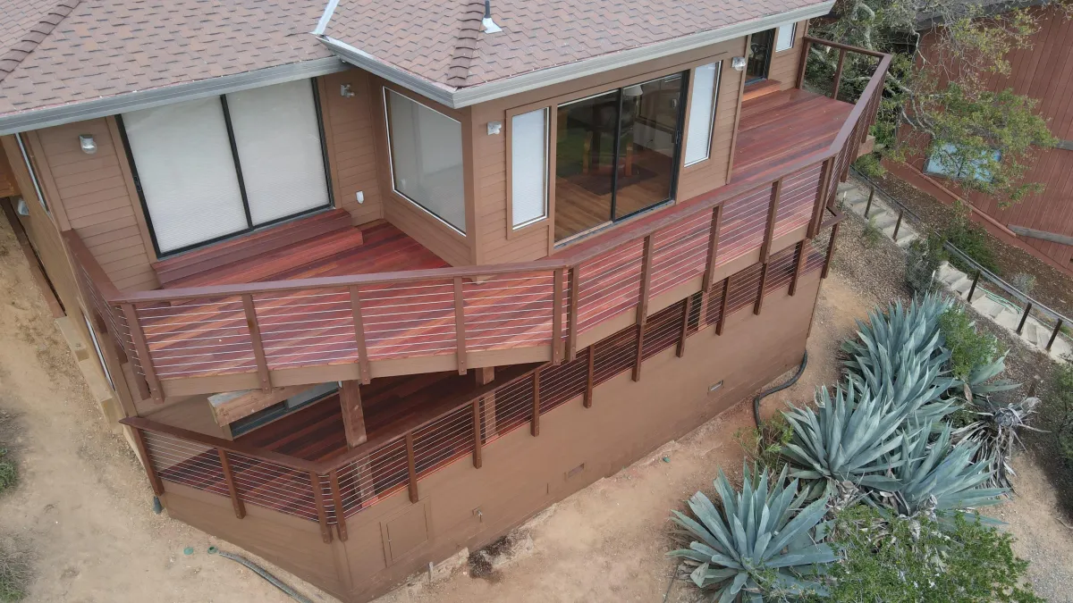 Two-story deck construction featuring tropical hardwood decking, cable railings, and a rich red finish using Sherwin-Williams SuperDeck stain.