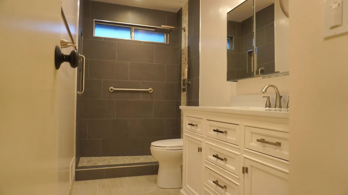 Bathroom remodel with grey tile walls, grab bar, and white toilet and vanity in Novato, CA