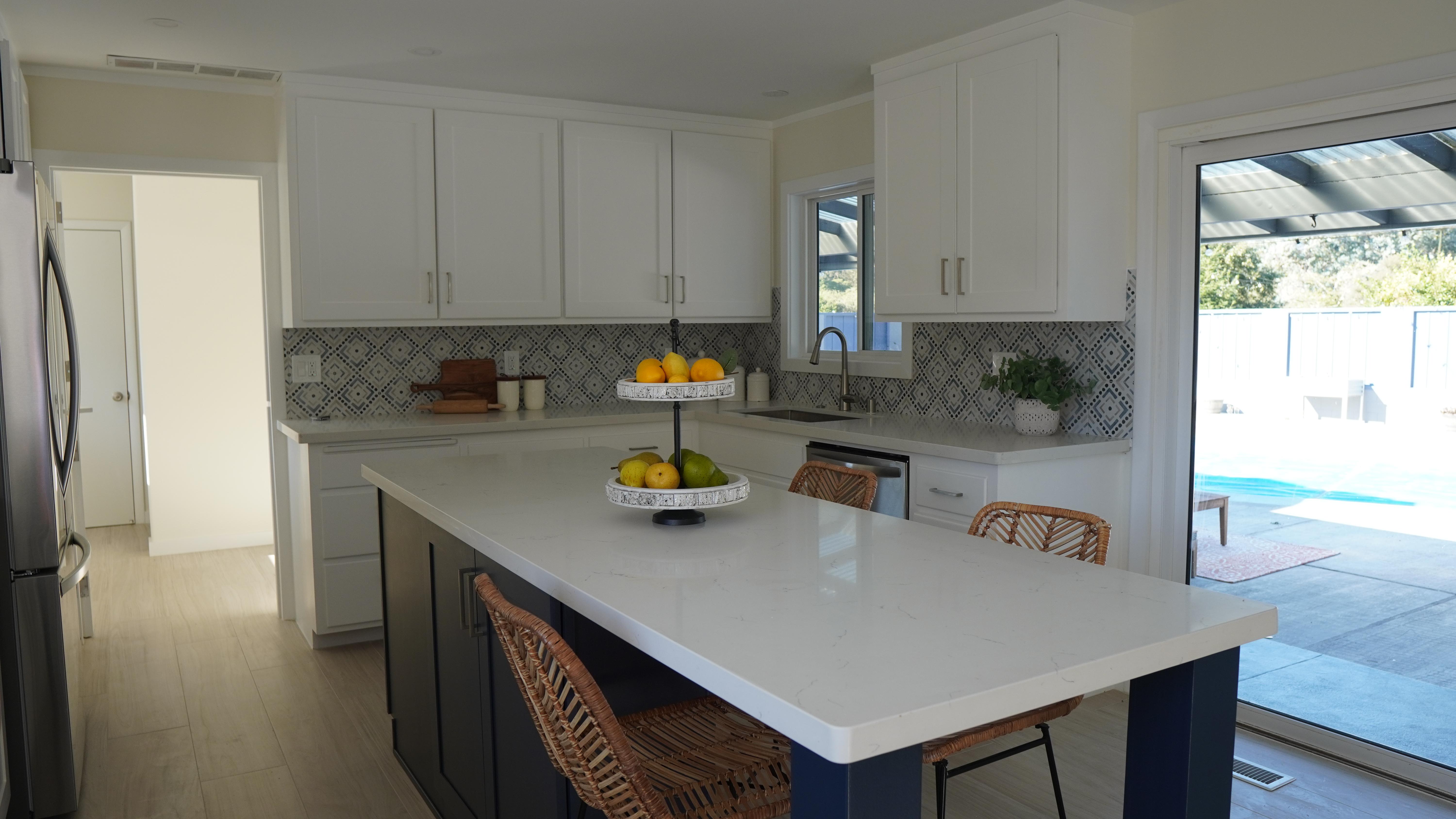 Kitchen Remodel featuring an kitchen island with white quartz countertops, white cabinets with stain-less steel hardware, colorful backsplash, tile floors in Half Moon Bay CA.
