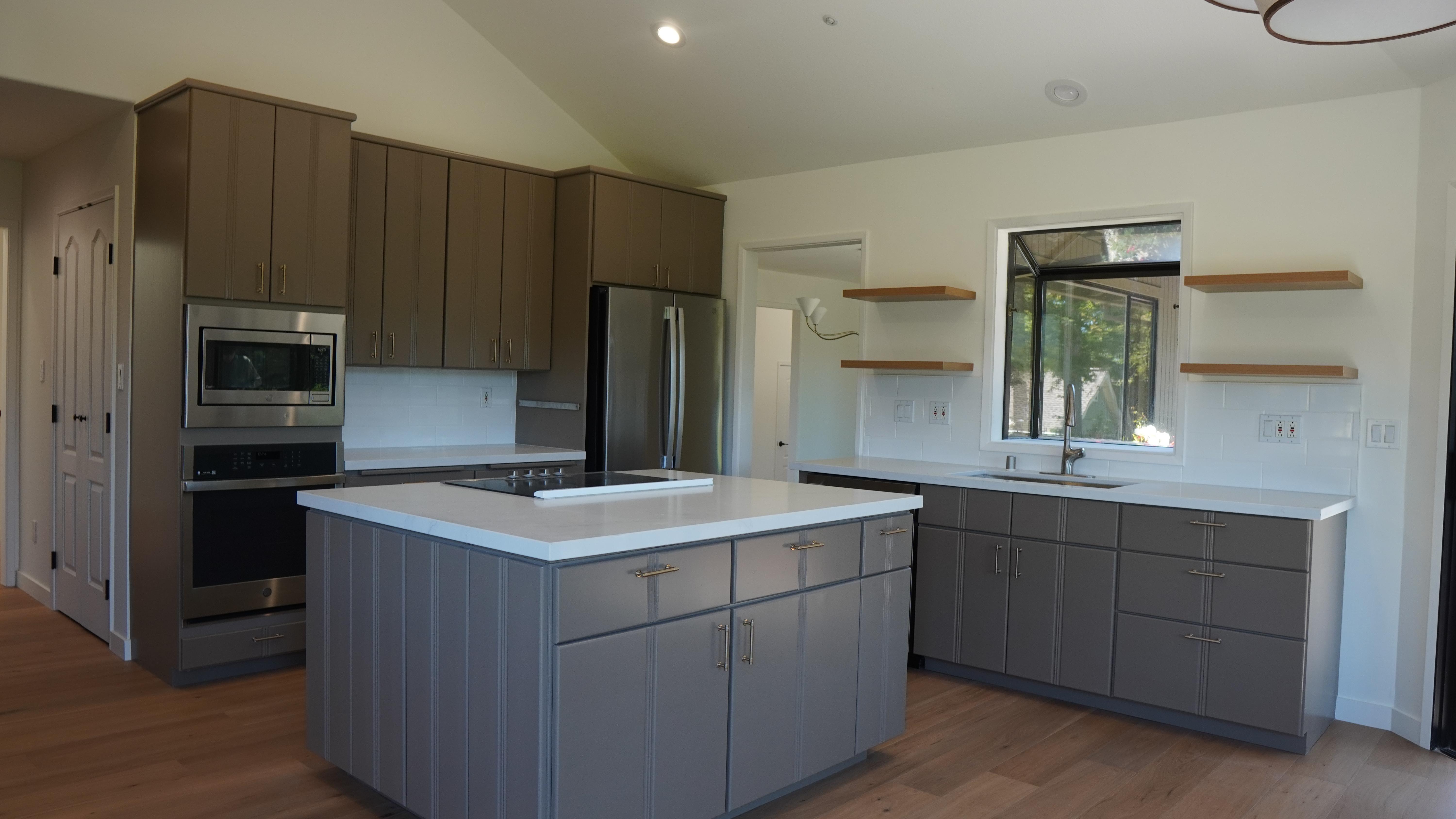 kitchen remodel featuring light grey island and base cabinets, dark grey wall cabinets, white countertops, floating shelve o both sides of the sink, hardwood flooring, stainless steel finish appliances in Novato, CA.