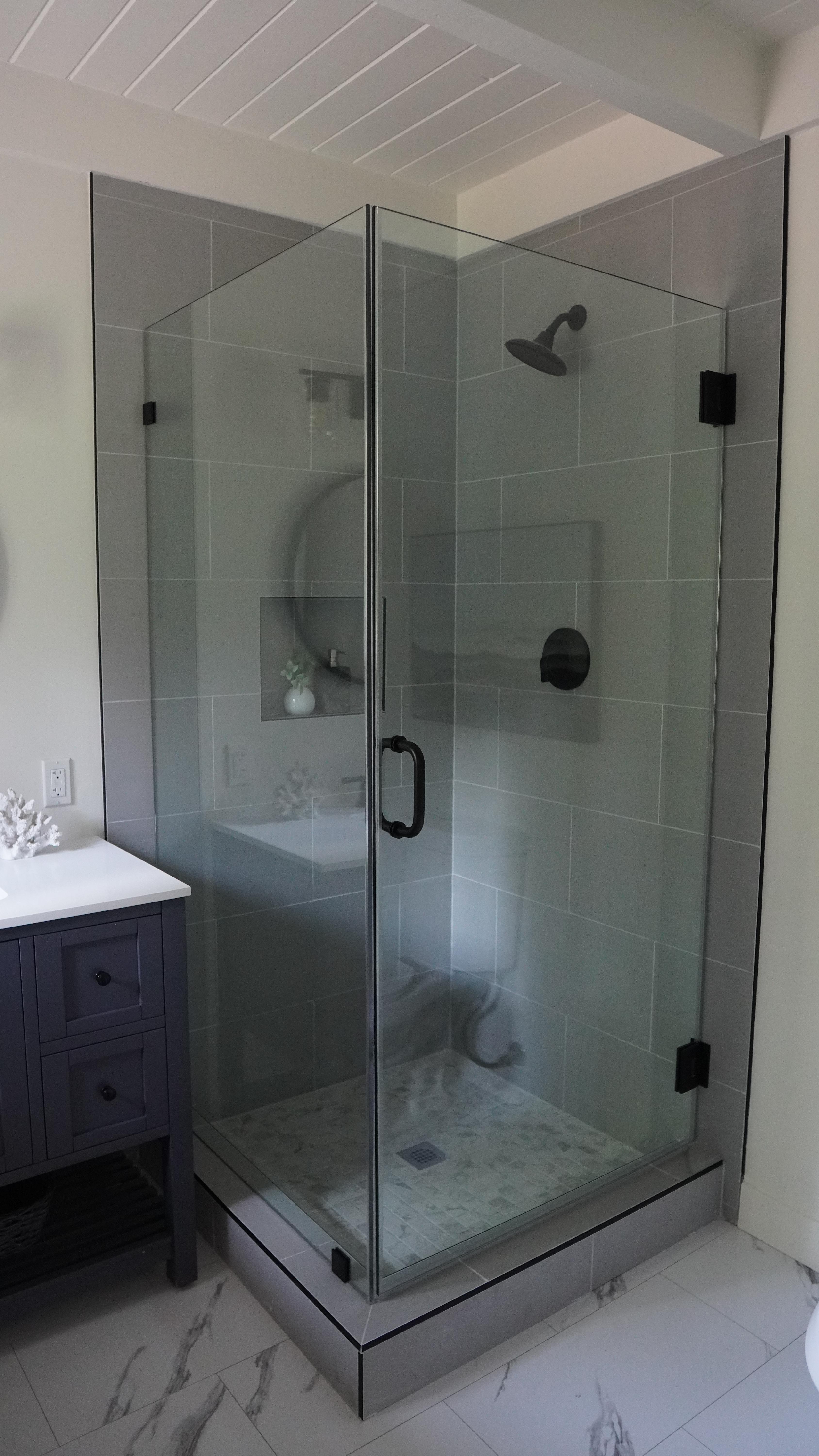 Bathroom remodel featuring shower glass door and panel, grey horizontal tile installation and black plumbing fixtures in Mil Vally CA.
