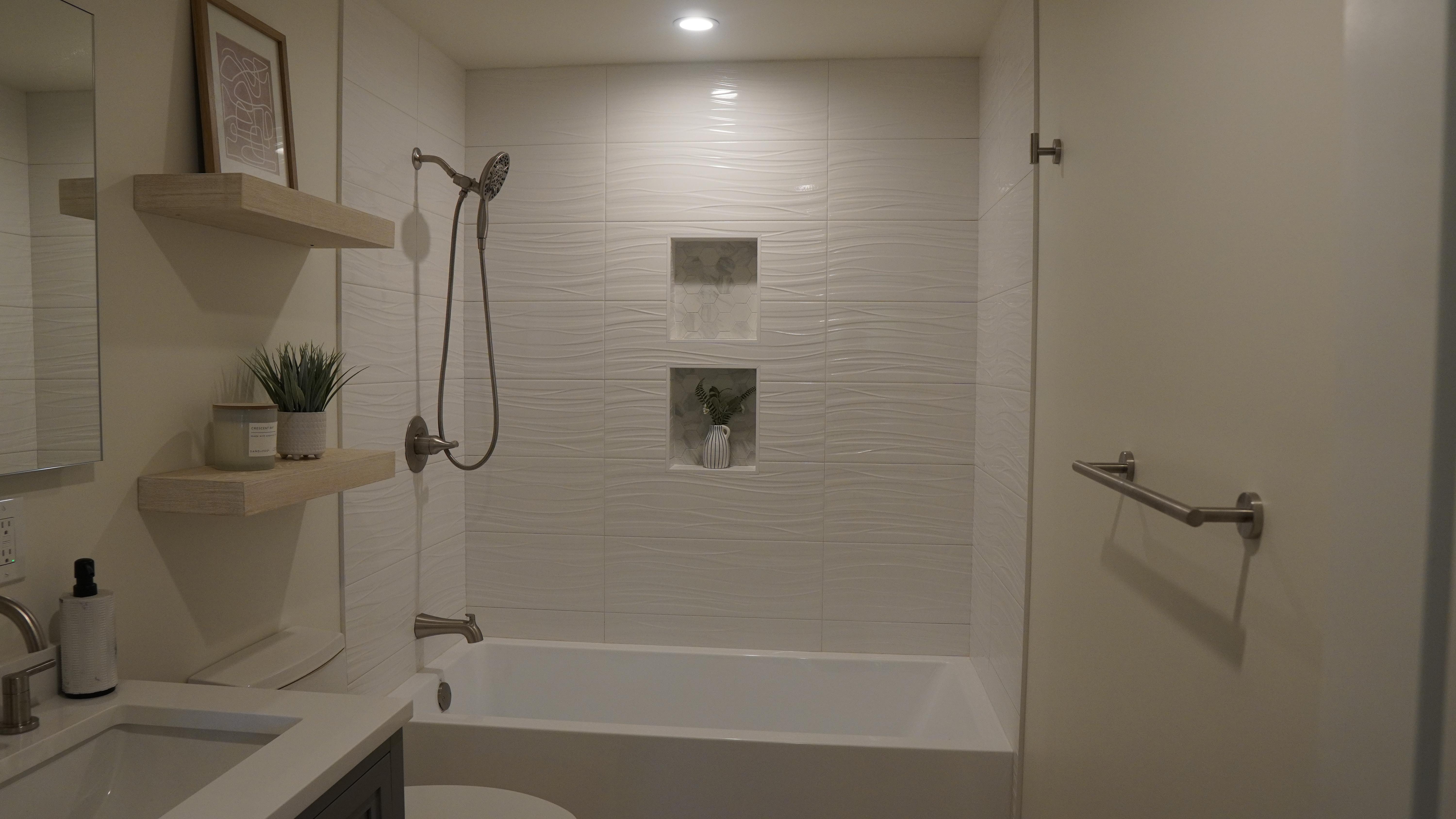 Bathroom remodel with white tile, double shampoo niche, white tube with hand held shower head, floating shelves, towel bar in San Francisco.