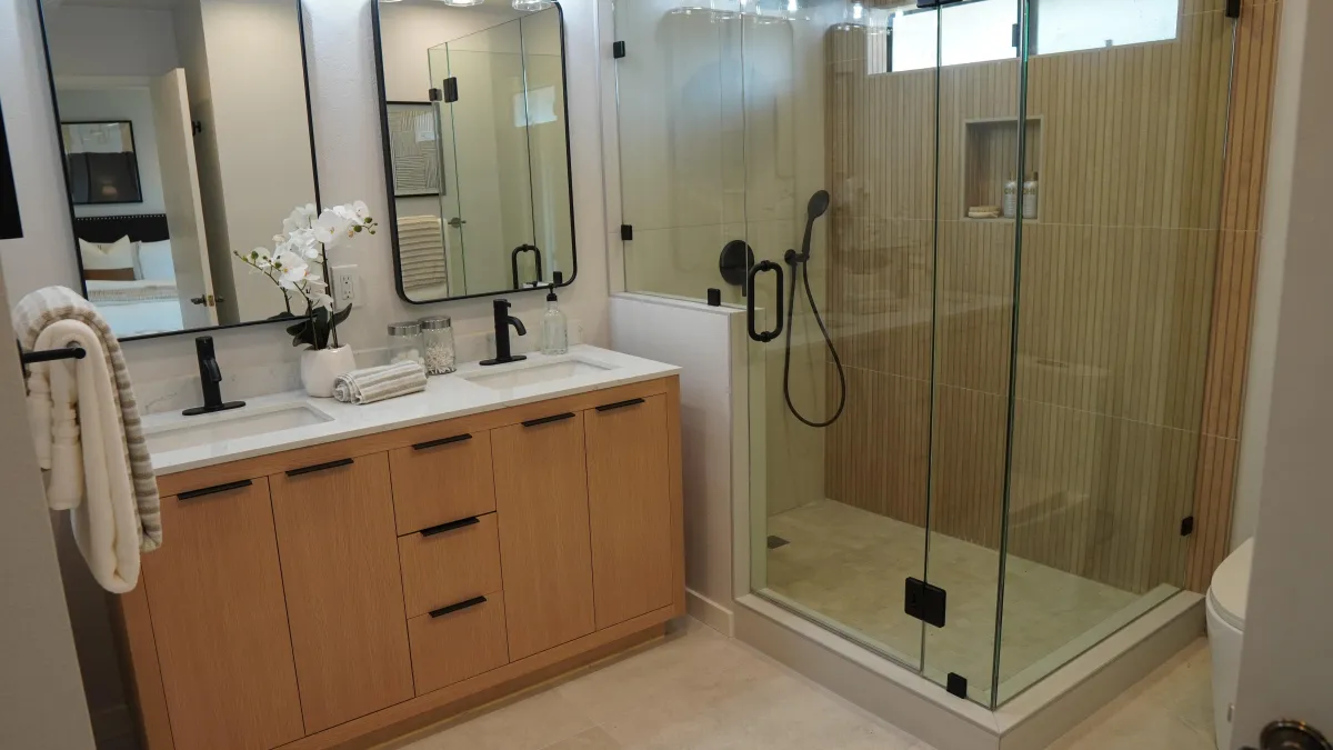 Bathroom remodel in San Carlos, California, featuring a walk-in glass shower, double wood vanity, matte black fixtures, and LED mirrors.