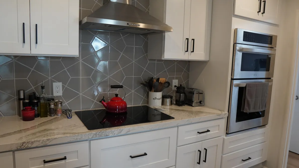 Kitchen remodel featuring white shaker cabinets with black hardware, Calacata countertops, grey tile backsplash in Daly City CA.