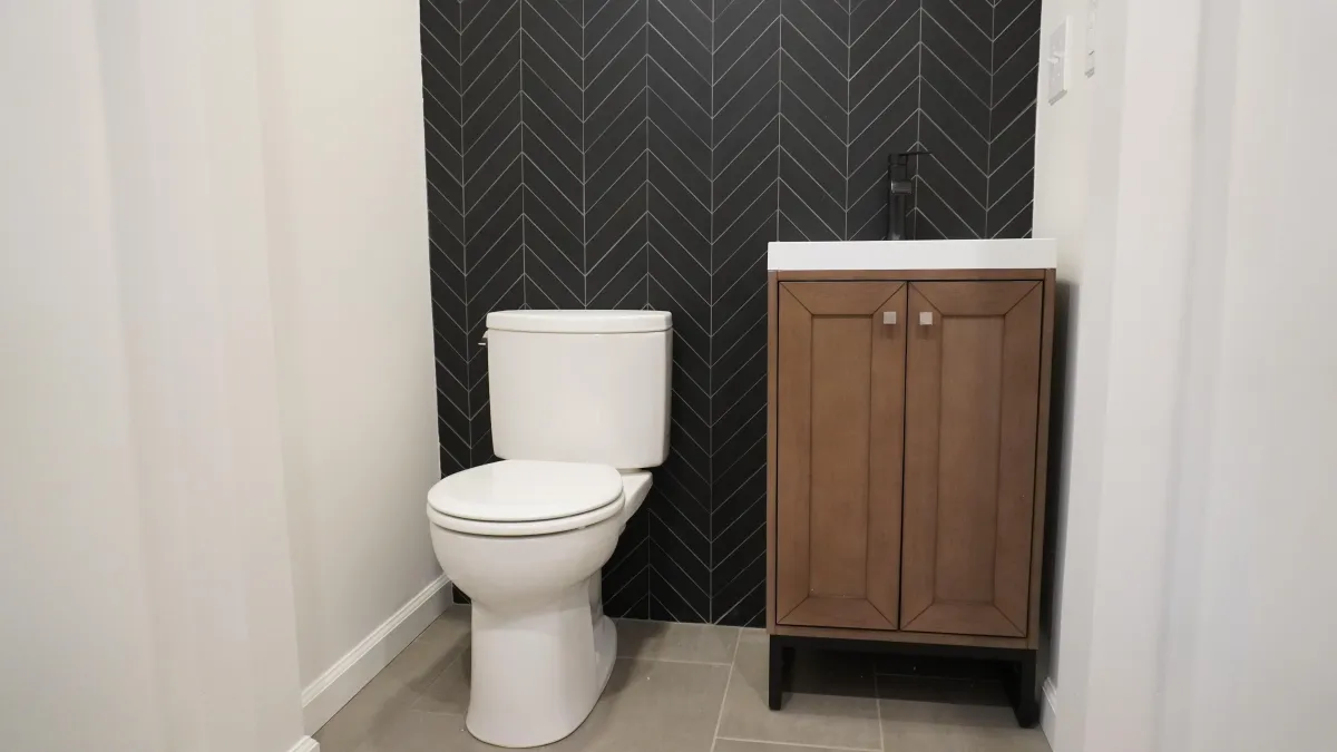 Pouter room with small vanity, white toilet and black tile wall in Mill Valley CA.