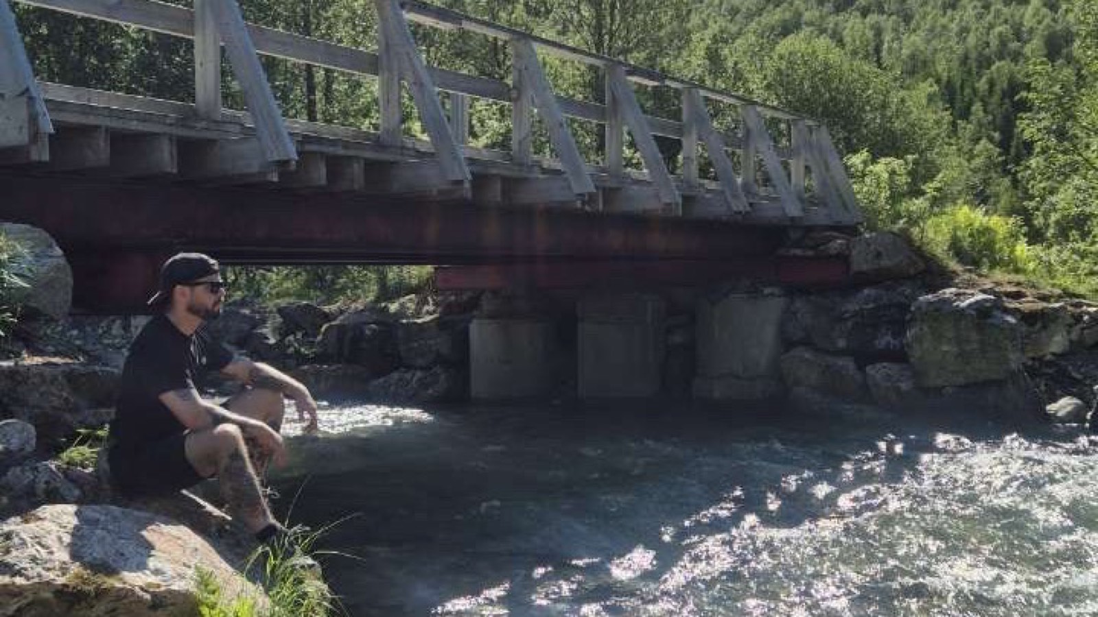 Johan Vesters sitting by a river under a wooden bridge in the Norwegian mountains