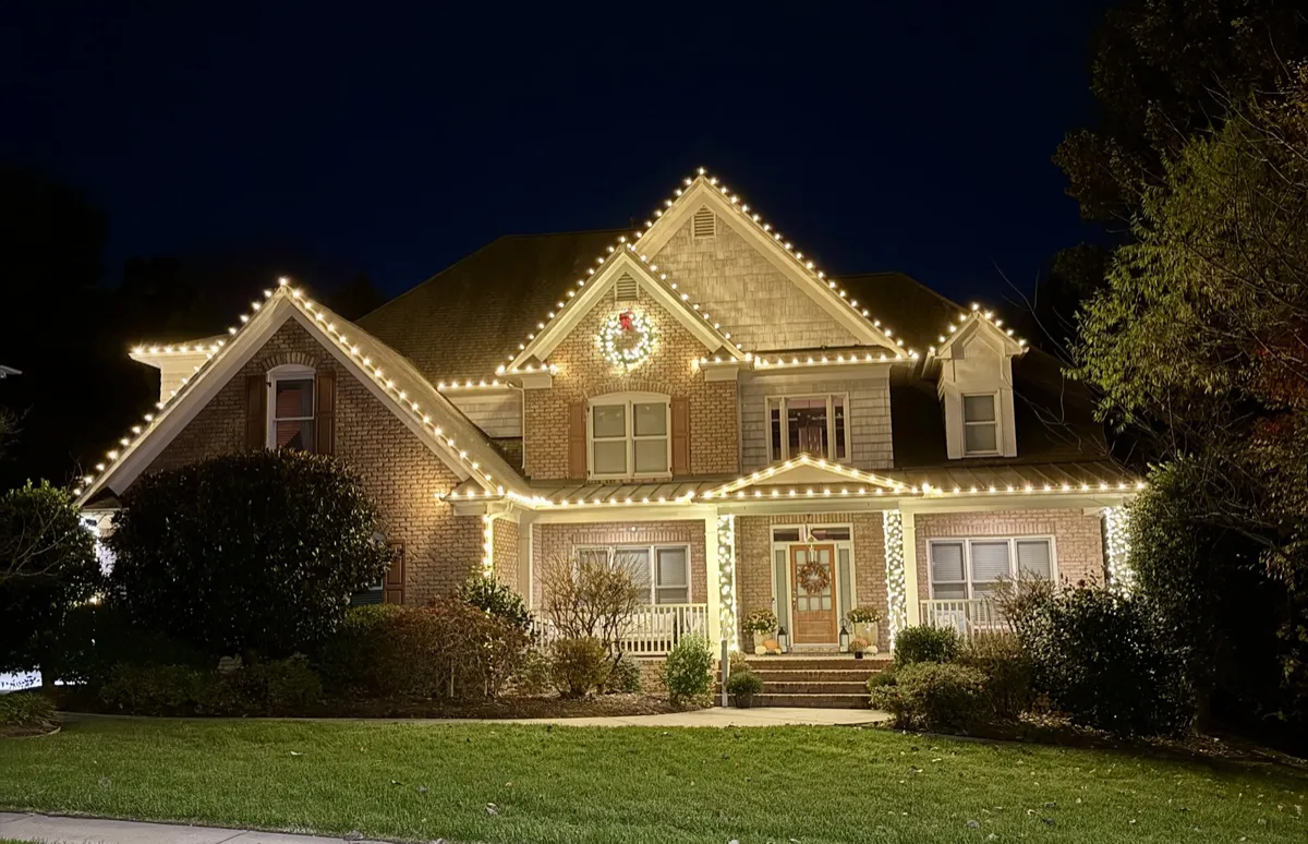 Two-story brick home in Harrisburg with warm white Christmas lights on every roofline