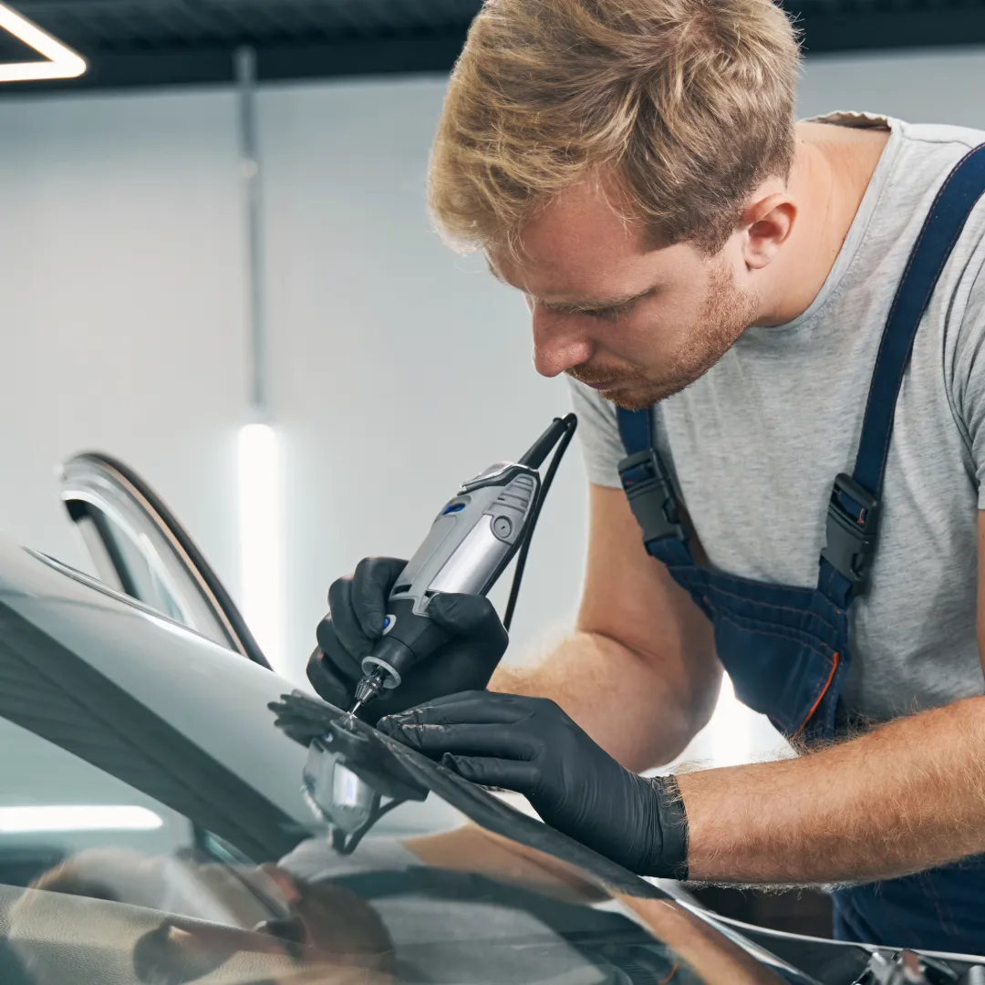 An experienced auto glass repair specialist using precision tools to fix a windshield crack.