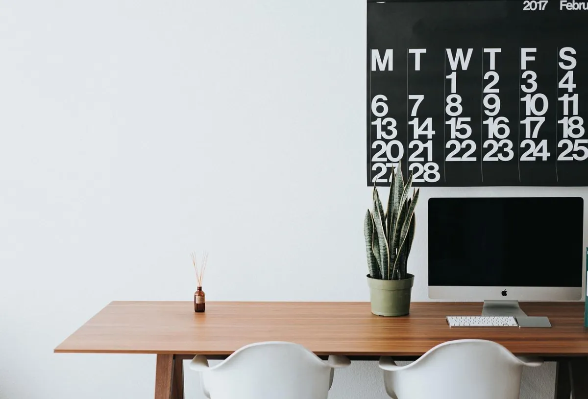 A table with a computer on it and a calendar on the wall
