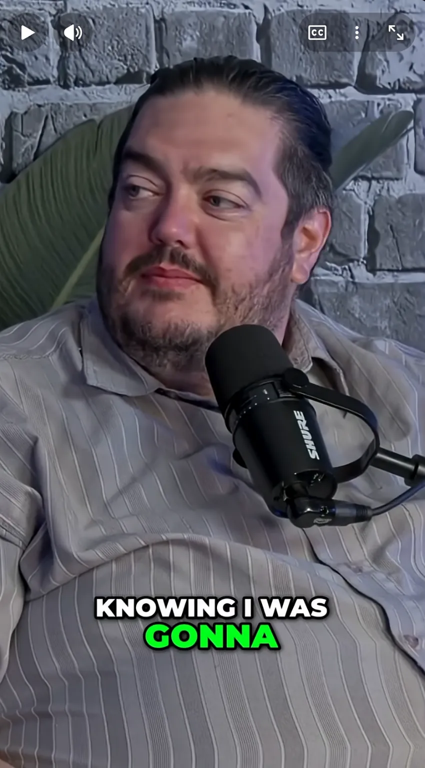 A broadcast microphone with a foam windscreen in the A Squared studio, against exposed brick and a plant