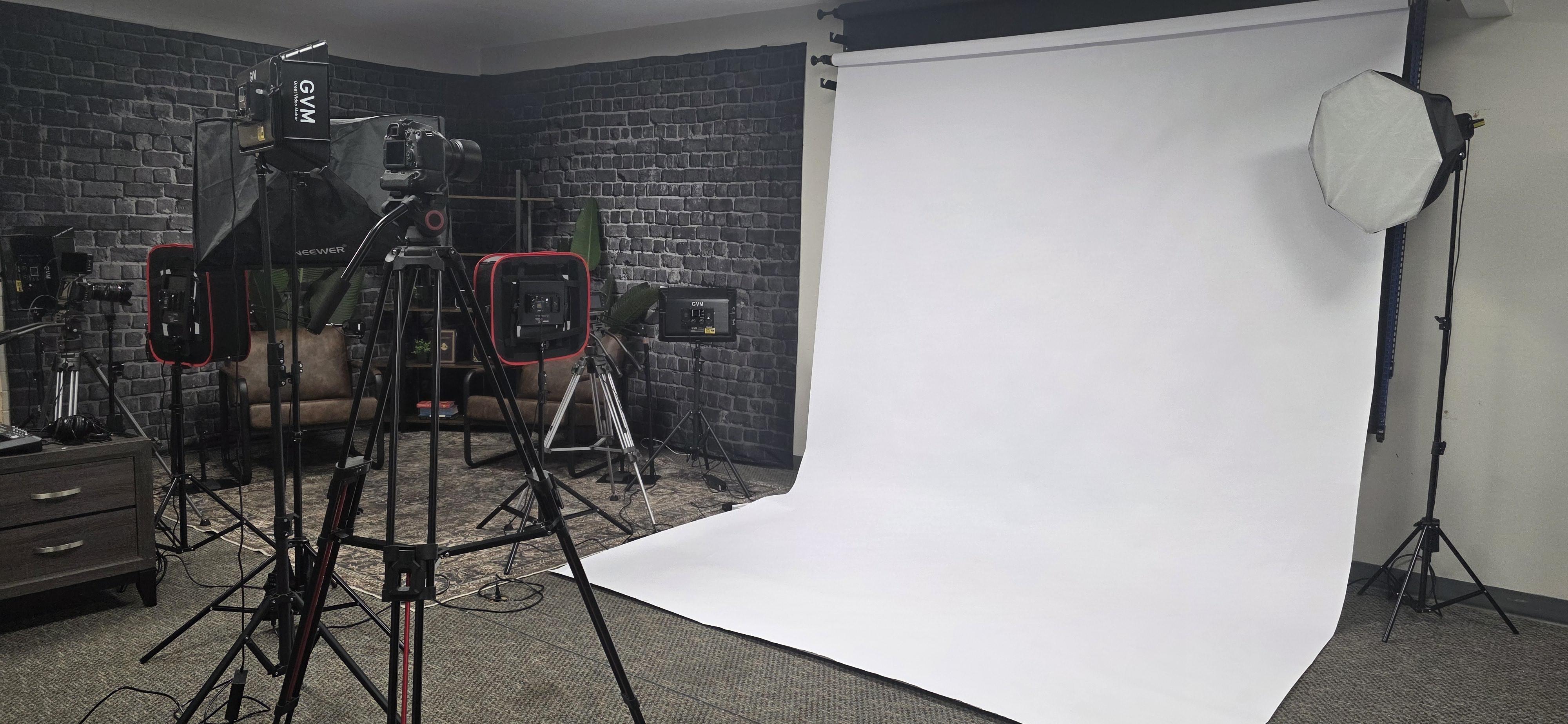 A Squared's podcast and video production studio in Fairfield, California, with two leather chairs, boom-arm microphones and studio lighting against an exposed brick backdrop. Pictured with our white paper backdrop available in the same space