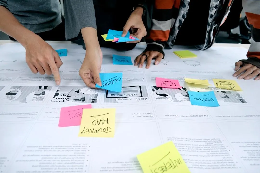 A widescreen image showing a team of professionals gathered around a conference table, reviewing charts and dashboards on a laptop. The focus is on hands, documents, and teamwork rather than faces. Bright neutral lighting, modern organizational setting, slight blur in the background for depth.