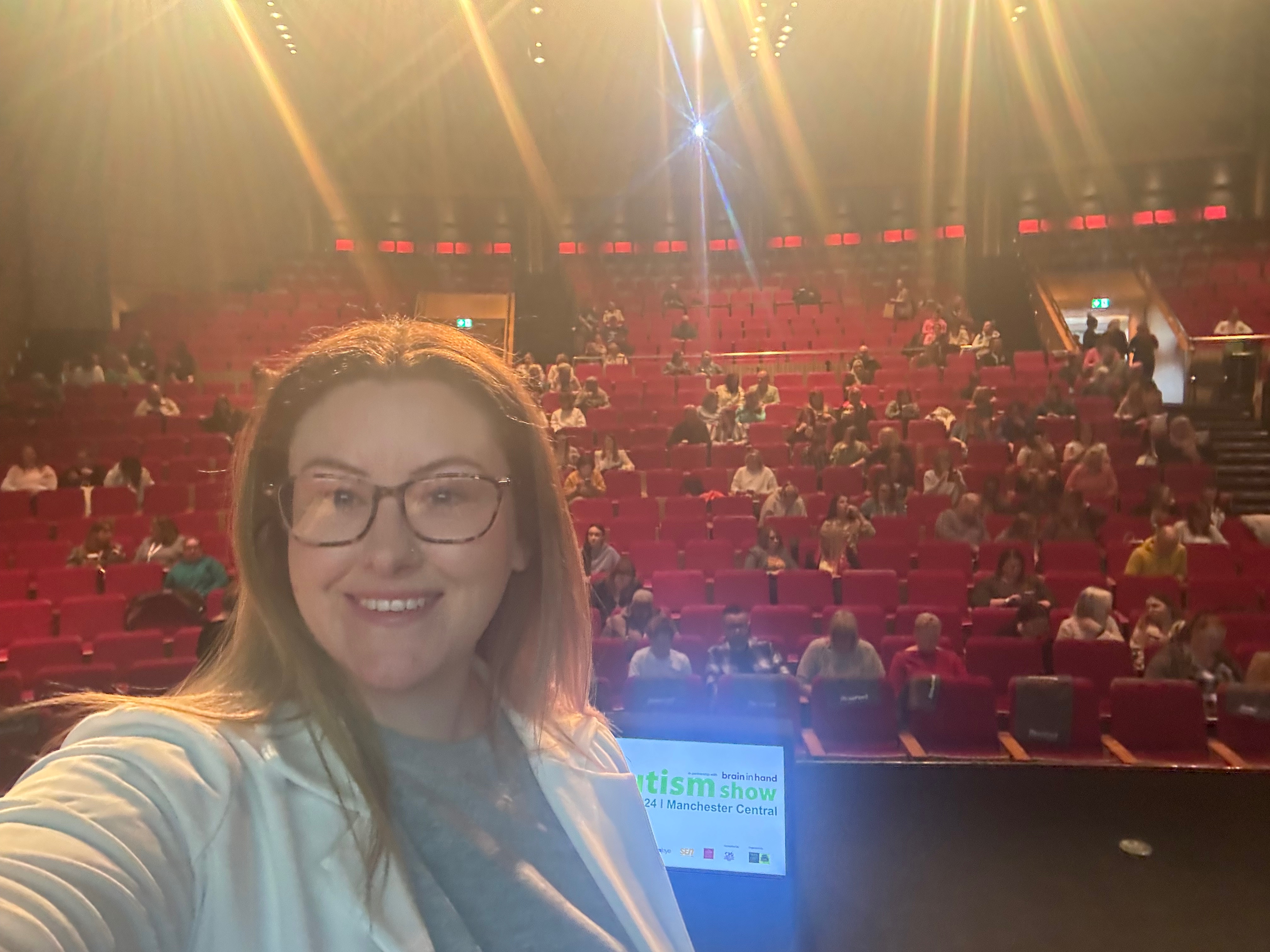 A young girl with curly dark hair, aged about 9, sits cross-legged on a patterned rug in a softly lit bedroom, reading a chapter book. She is focused and calm, surrounded by colourful cushions and a small bookshelf. The scene conveys independence and comfort, with gentle pastel tones throughout.