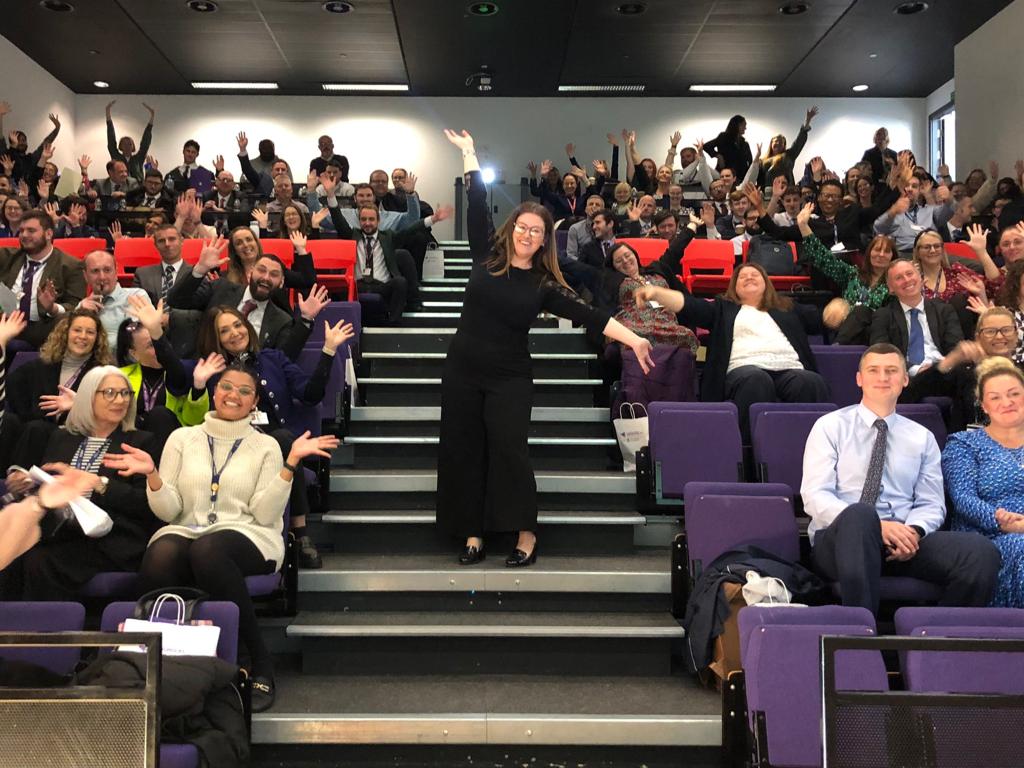 A professional portrait of Dr. Emily Carter, a woman in her early 40s with short auburn hair and glasses, wearing a navy blazer and a soft blue blouse. She stands against a blurred bookshelf background, smiling warmly, conveying expertise and approachability.