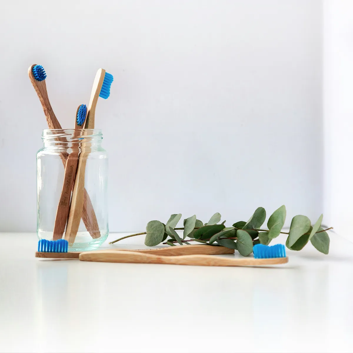 Toothbrushes in a glass beside fresh greenery
