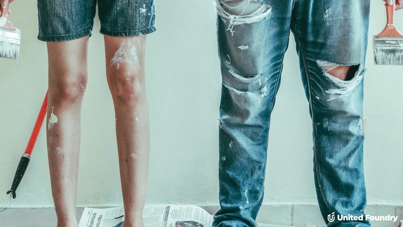 Paint-splattered couple holding brushes during a DIY home renovation