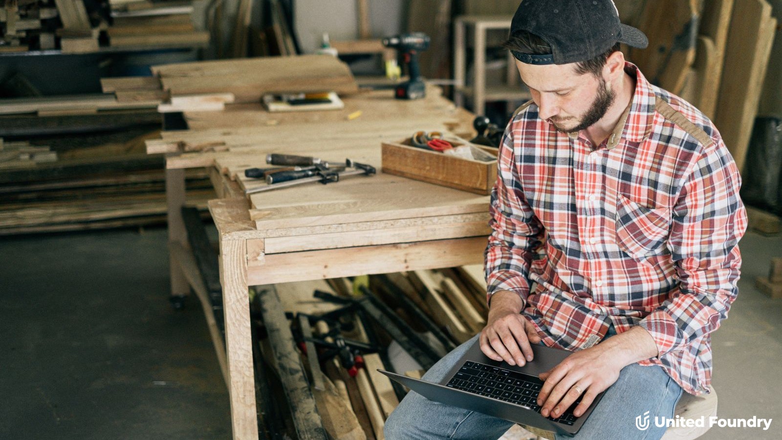 Contractor sitting in a workshop using a laptop next to a workbench of tools
