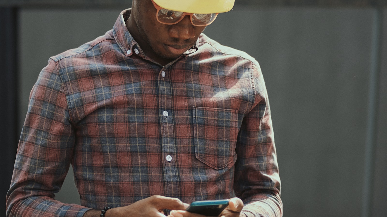 Contractor in a hard hat and safety glasses sending a follow-up text message on his phone at a job site