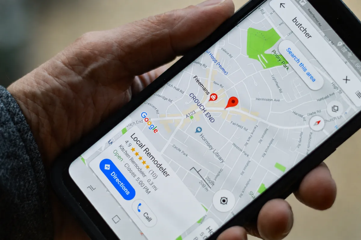 Hand holding a phone showing a Google Maps local search with a business listing, star rating, and call button — the Google Business Profile in action