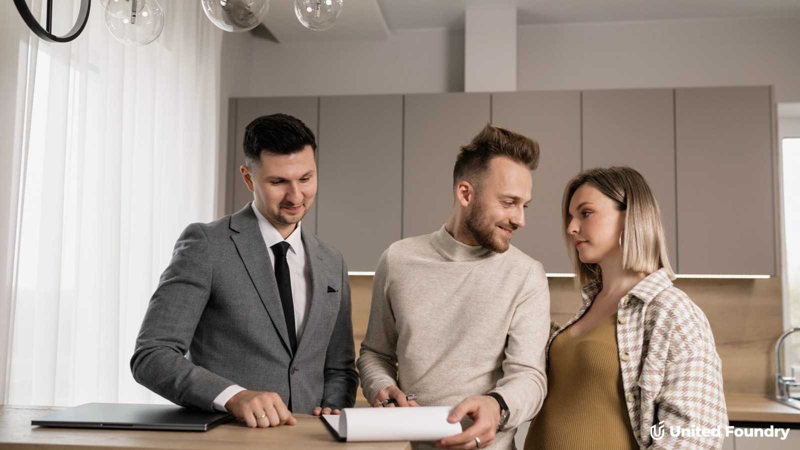 A contractor reviewing a written proposal and budget with two homeowners around the island of a newly finished kitchen