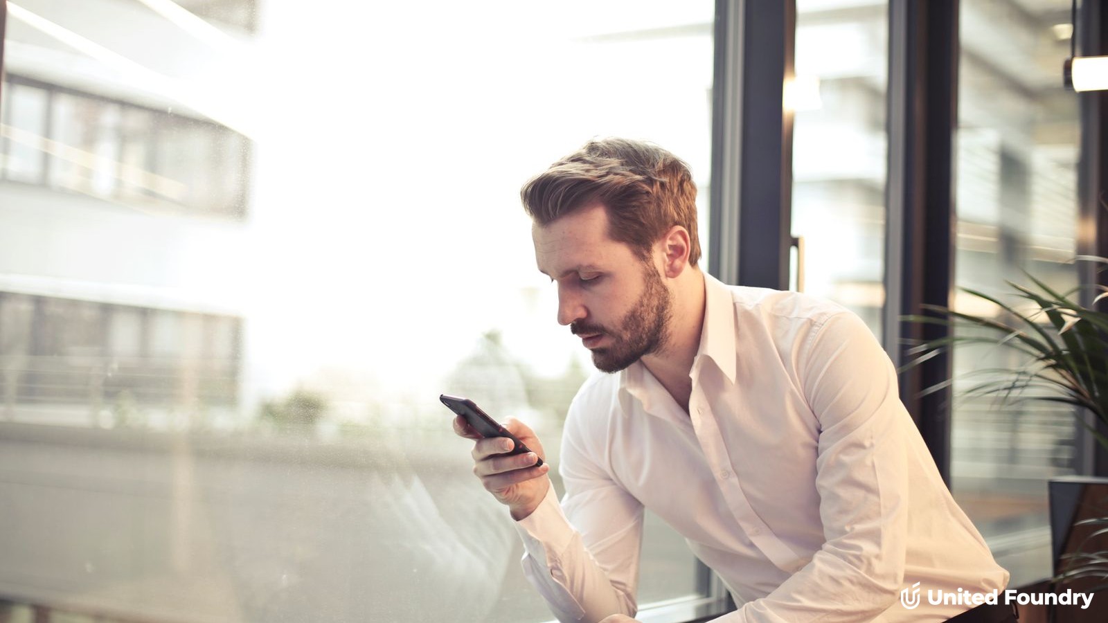 Business owner reading a text message on his smartphone by an office window