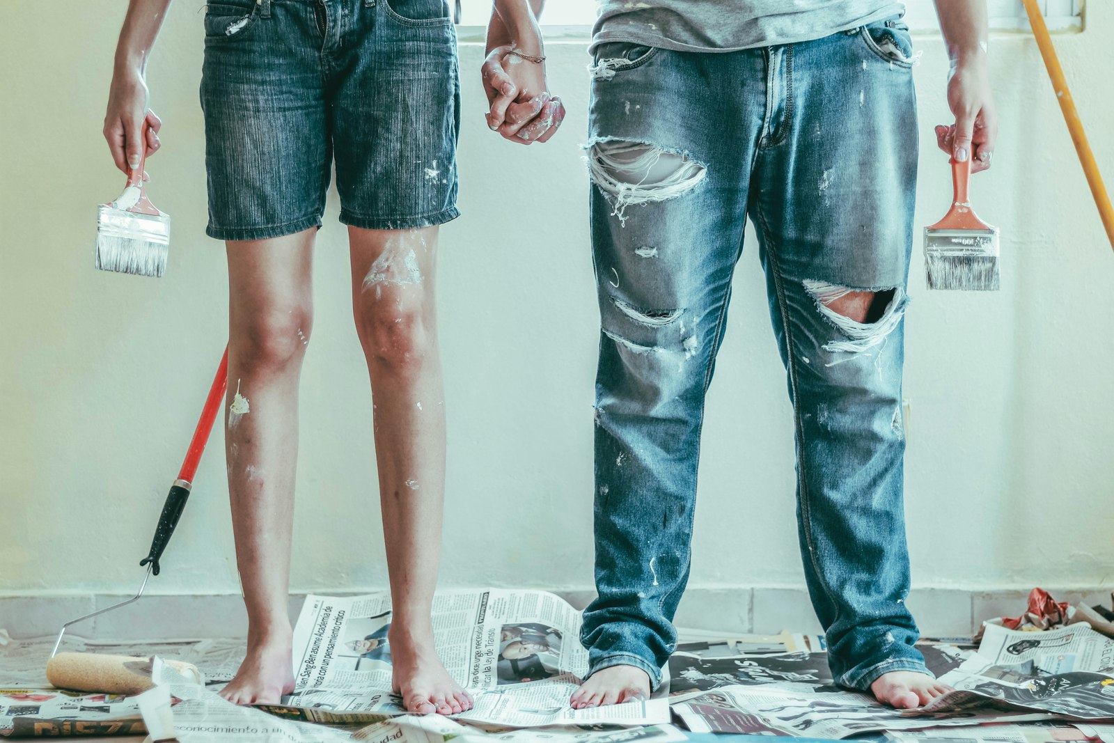Paint-splattered couple holding brushes during a DIY home renovation