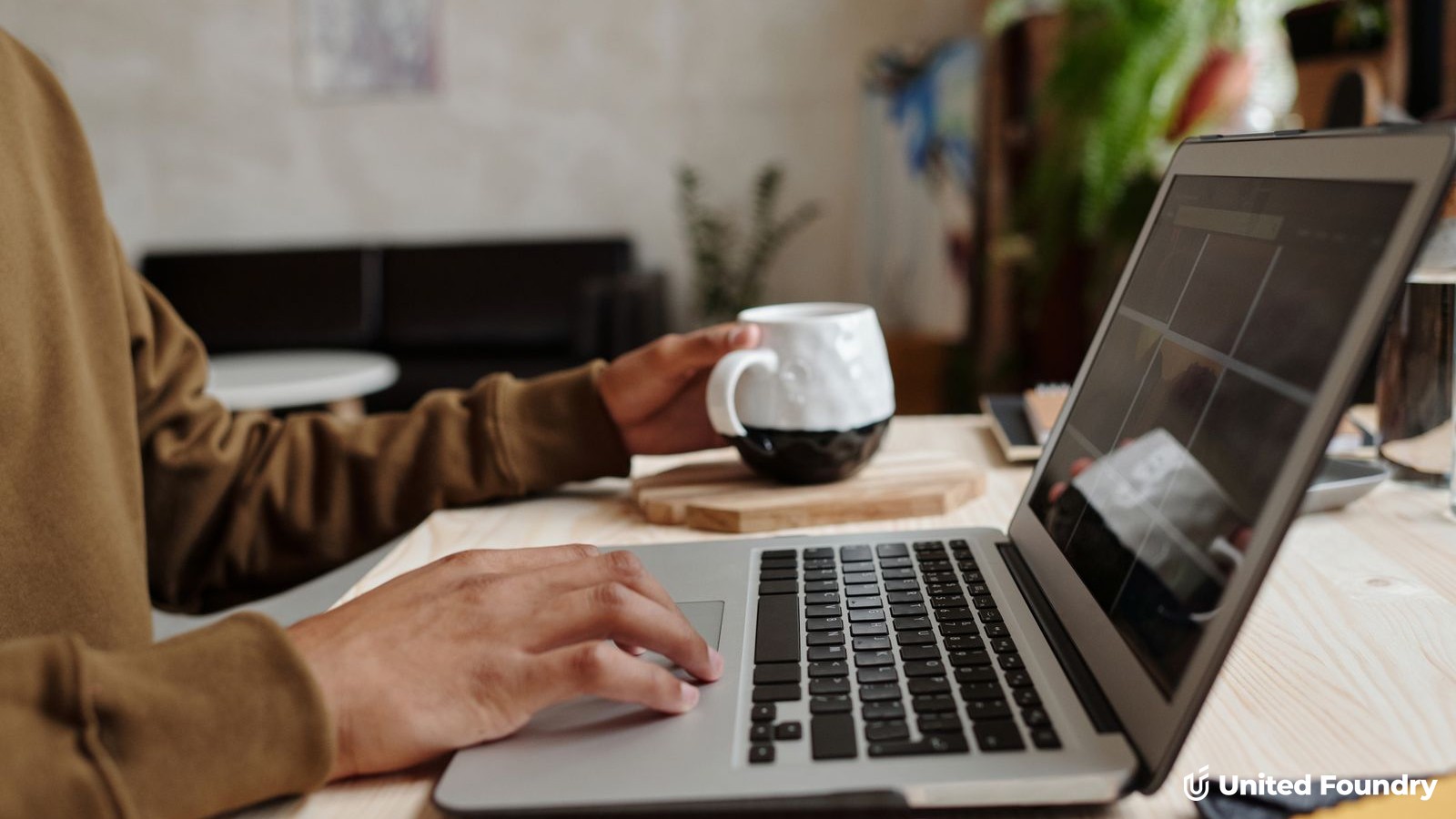 Person at a laptop viewing a website homepage layout, coffee mug beside them