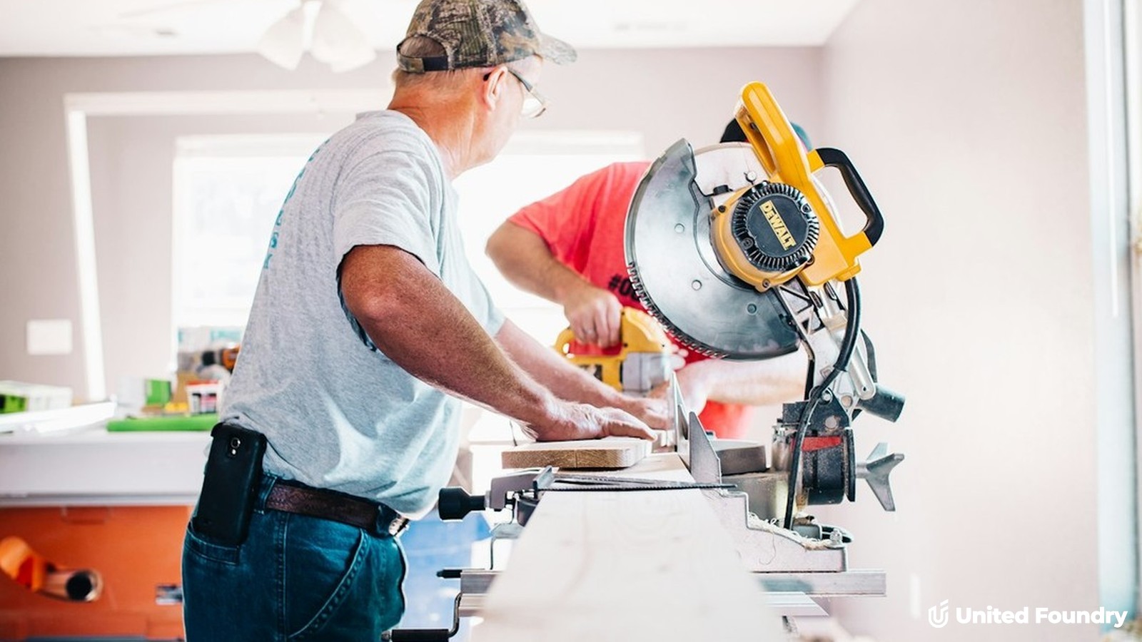 Two remodeling contractors cutting trim with a miter saw inside a home renovation
